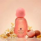 A pink Her Wisdom skin & hair perfume mist bottle with a rounded spherical cap, surrounded by white flowers, lychee fruits, and amber pieces on a soft peach background.